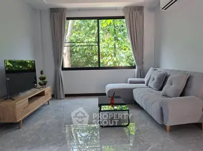 Modern living room with large window and stylish furniture, offering a serene view of lush greenery.