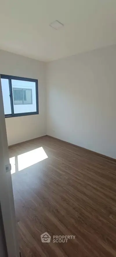 Spacious empty room with wooden flooring and large window, ideal for customization.