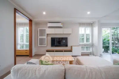 Spacious modern living room with natural light and garden view, featuring cozy seating and sleek entertainment center.