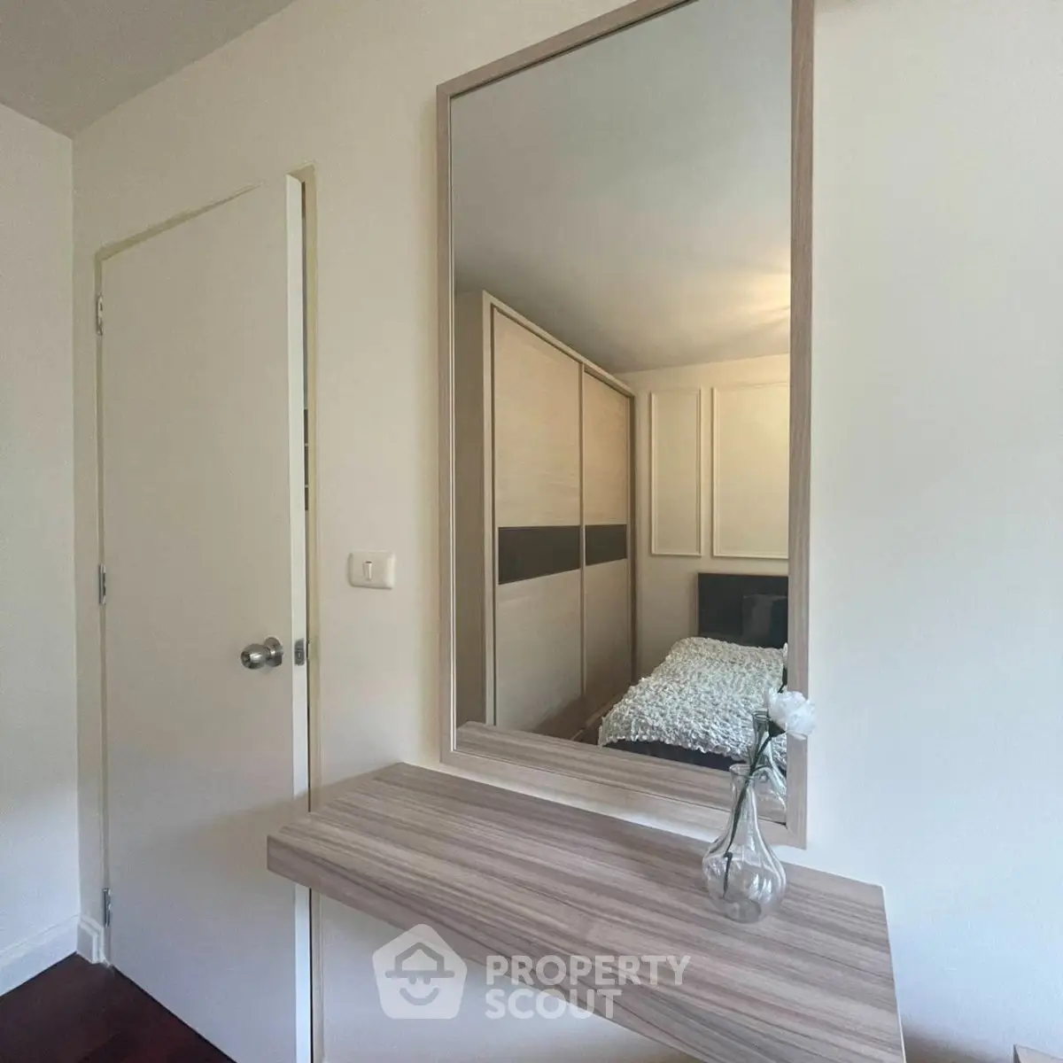 Cozy bedroom with modern decor and large mirror reflecting a stylish wardrobe.