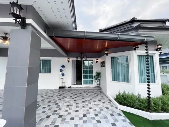 Modern single-story house with stylish entrance and tiled driveway, featuring contemporary design and lush greenery.