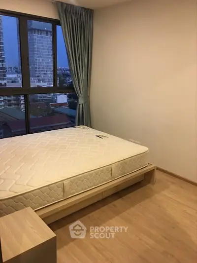 Cozy bedroom with large window offering city view, featuring a comfortable bed and wooden flooring.