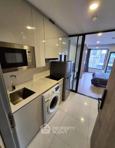 Modern compact kitchen with appliances and view into bedroom in urban apartment