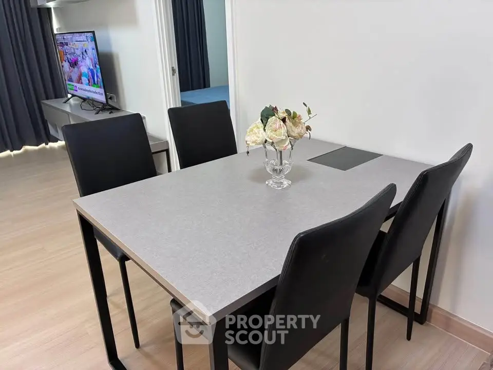 Modern dining area with sleek table and chairs, adjacent to a cozy living room with TV.