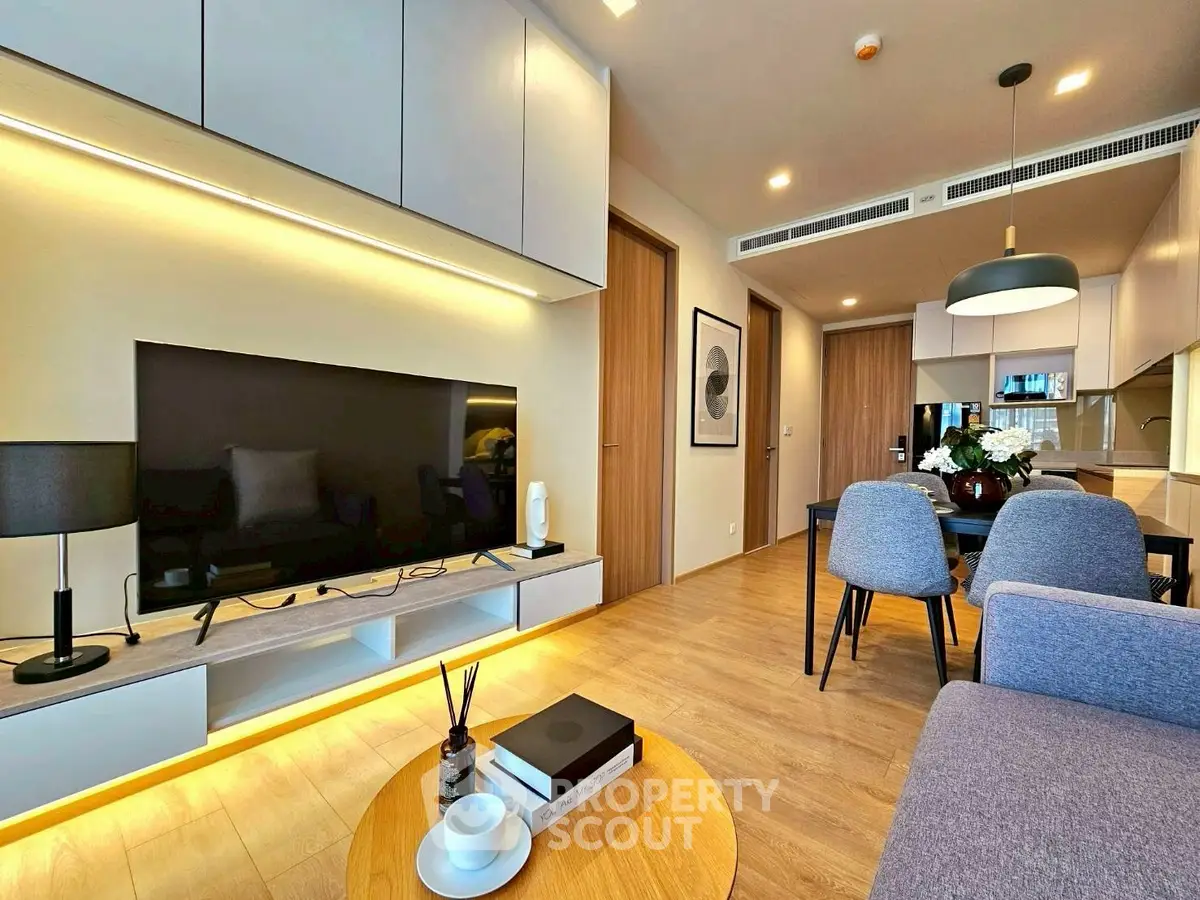Modern living room with sleek furniture and open dining area, featuring a large TV and stylish decor.