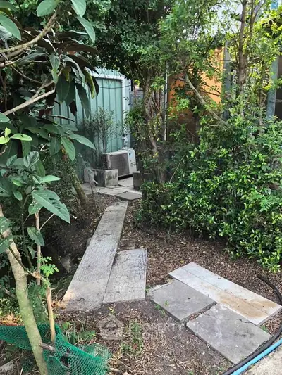 Charming garden pathway surrounded by lush greenery and outdoor air conditioning unit.