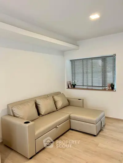 Modern living room with beige sectional sofa and large window with blinds.