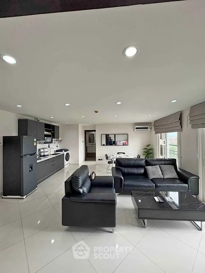 Spacious modern living room with sleek black furniture and open kitchen layout