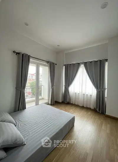 Spacious bedroom with large windows and balcony access, featuring elegant curtains and wooden flooring.