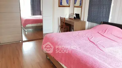 Cozy bedroom with pink bedding and wooden flooring, featuring a mirrored wardrobe and desk.