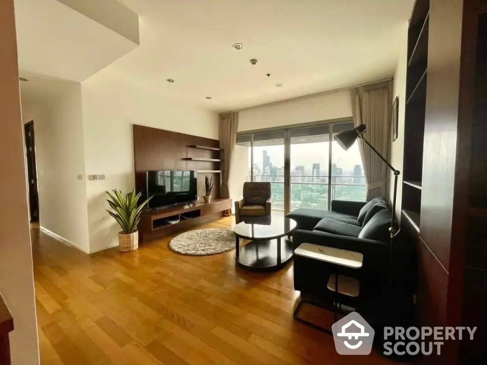 Spacious living room with polished hardwood floors, modern furniture, and abundant natural light from floor-to-ceiling windows offering a cityscape view.