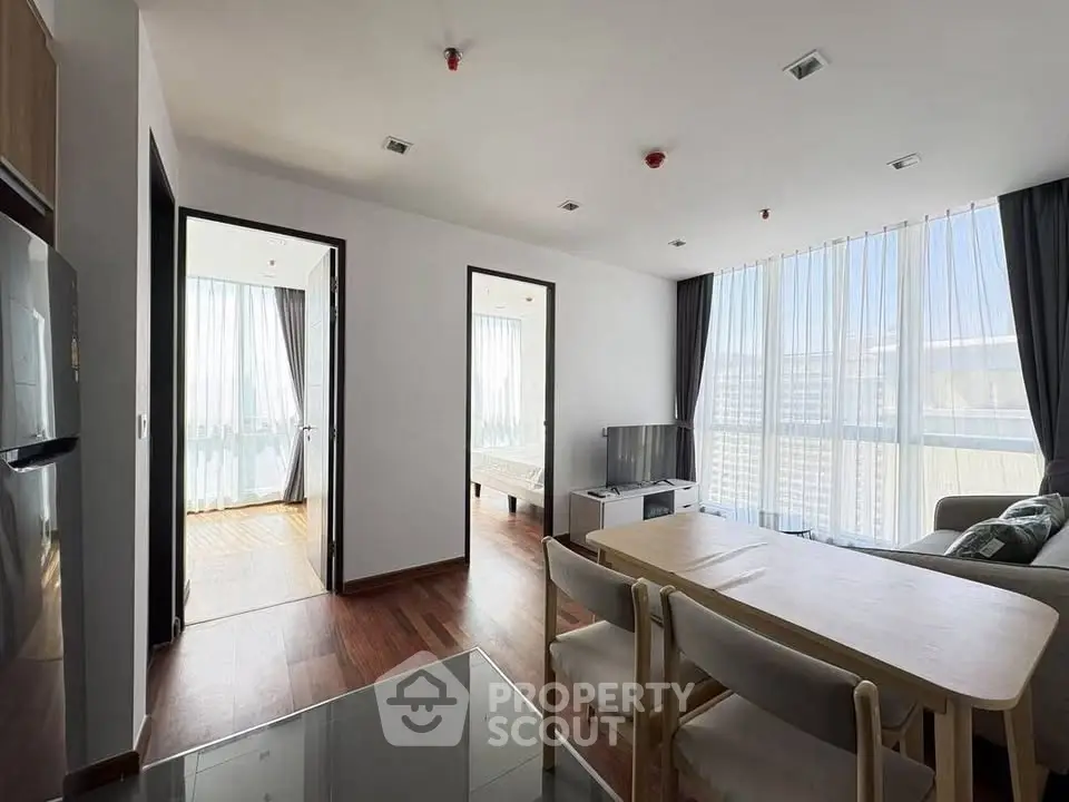 Modern apartment interior with open living and dining area, featuring large windows and natural light.