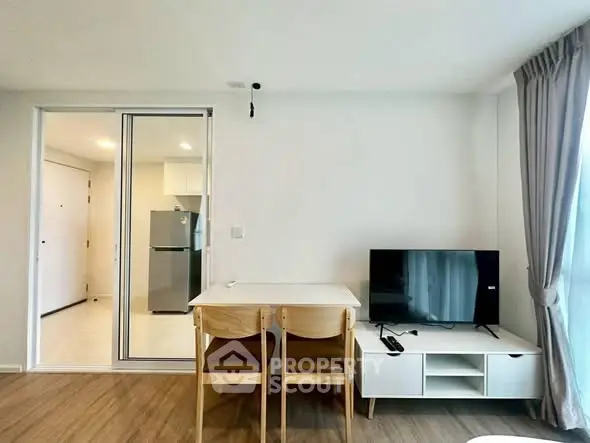 Modern living room with dining area and TV, featuring sleek furniture and natural light.