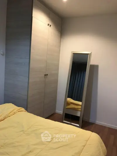 Cozy bedroom with wooden wardrobe and full-length mirror, featuring a warm yellow bedspread.