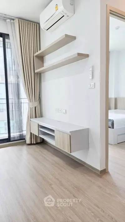 Modern living room with sleek shelving and air conditioning, featuring a view into a stylish bedroom.