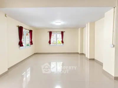 Spacious empty living room with glossy tiled floors and large windows with red curtains.