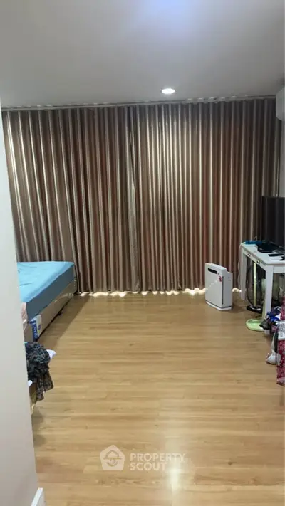 Spacious bedroom with wooden flooring and elegant curtains, featuring a cozy bed and modern desk setup.
