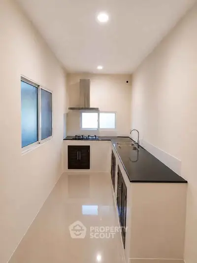 Sleek modern kitchen with black countertops and gas stove in a narrow layout