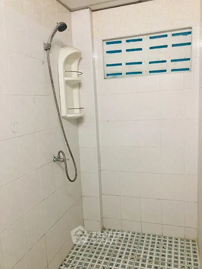 Minimalist bathroom with tiled walls and floor featuring a showerhead and built-in shelf.