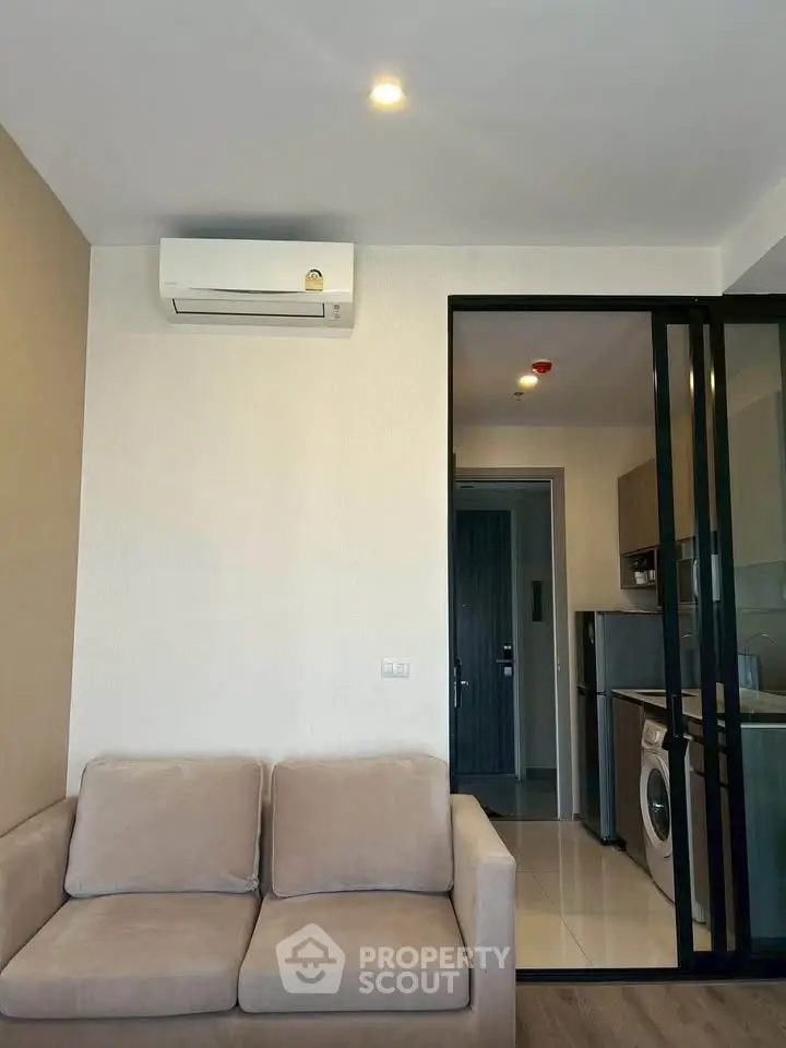 Modern living room with air conditioning and view into a sleek kitchen with washing machine.
