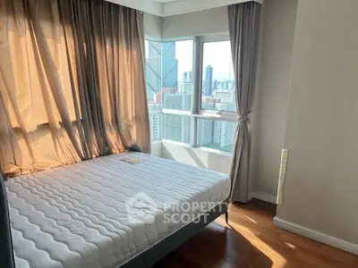 Bright bedroom with city view and large windows, featuring elegant curtains and wooden flooring.