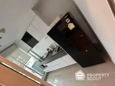 Modern kitchen with sleek black fridge and white cabinetry in stylish apartment.