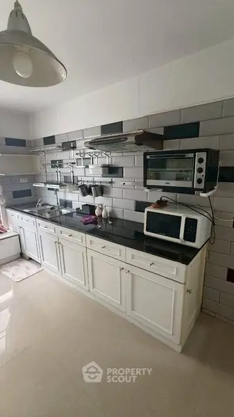 Modern kitchen with sleek white cabinets and black countertop, featuring a microwave and oven for convenient cooking.