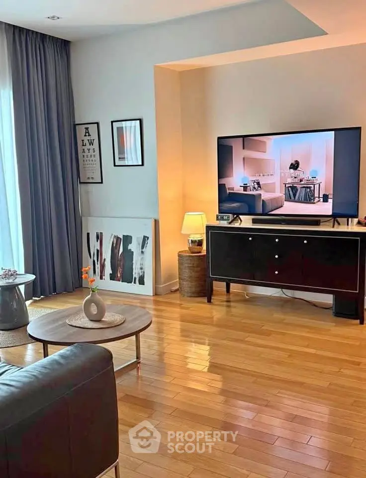 Stylish living room with modern decor and large TV, featuring wooden flooring and elegant curtains.