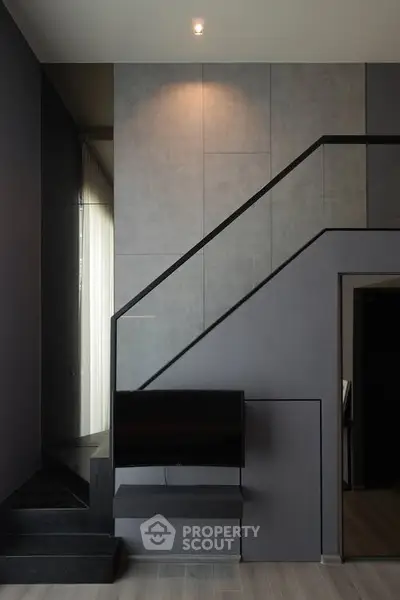 Modern minimalist interior with sleek staircase and wall-mounted TV in stylish living space.