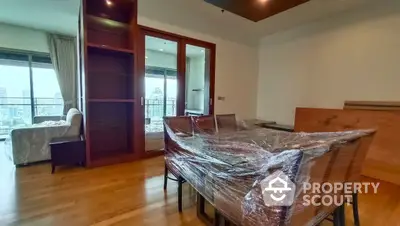 Spacious bedroom with polished wooden floors, large windows offering ample natural light, and a cozy sitting area leading to a sunny balcony.