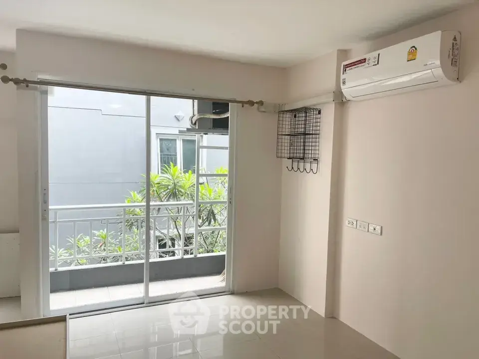 Bright living room with sliding glass doors leading to a small balcony, featuring air conditioning and modern decor.