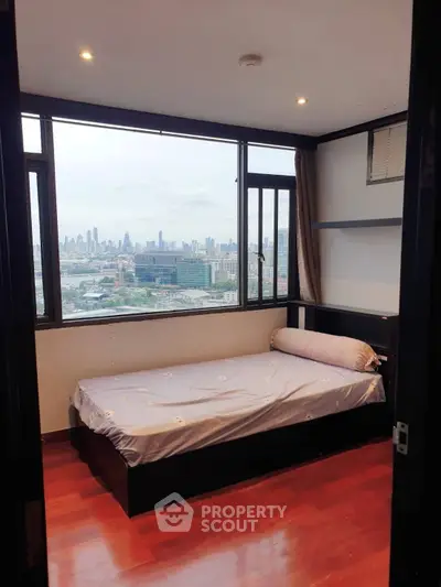 Cozy bedroom with stunning city view, featuring large windows and wooden flooring, perfect for urban living.