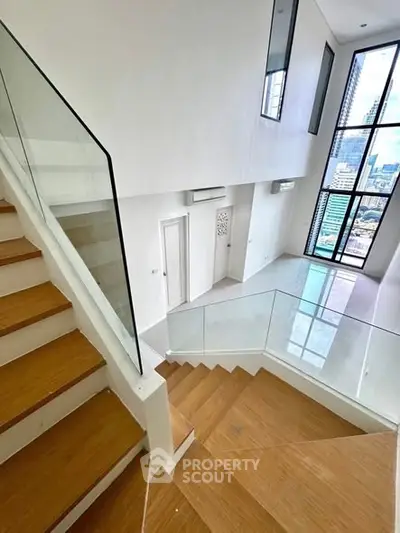 Modern duplex interior with wooden staircase and large windows offering city views.