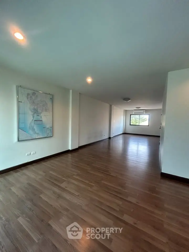 Spacious empty living room with wooden flooring and large window view.