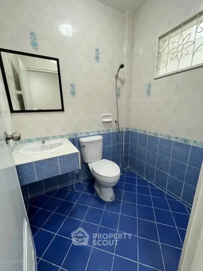 Modern bathroom with blue tile flooring and white fixtures, featuring a shower and sink.