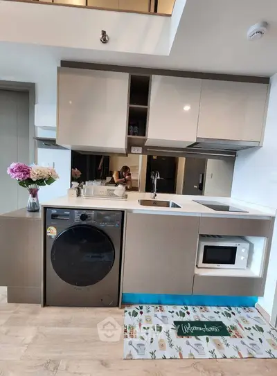 Modern kitchen with washing machine and microwave, sleek cabinets, and floral decor.