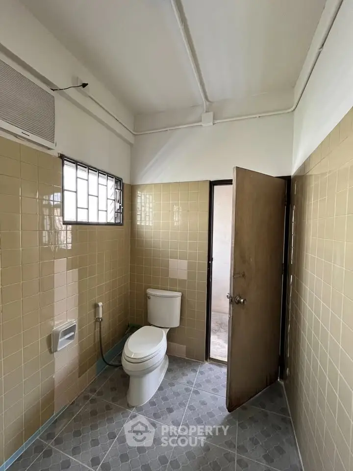 Spacious bathroom with beige tiles and natural light, featuring a modern toilet and classic design.
