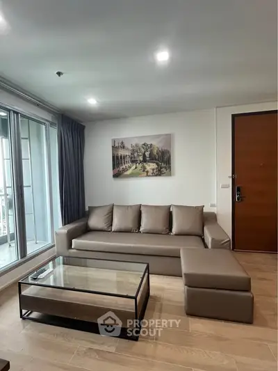 Modern living room with sleek sofa, glass coffee table, and balcony view in stylish apartment.
