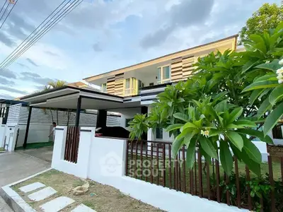 Modern two-story house with carport and lush garden in a serene neighborhood.