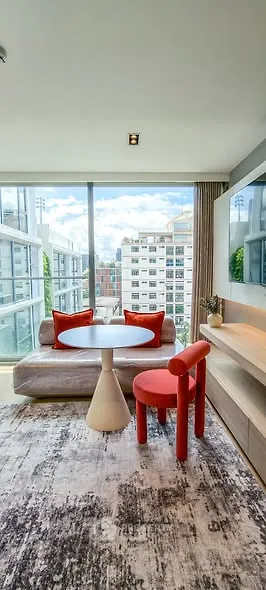 Modern living room with floor-to-ceiling windows and city view, featuring stylish furniture and vibrant decor.