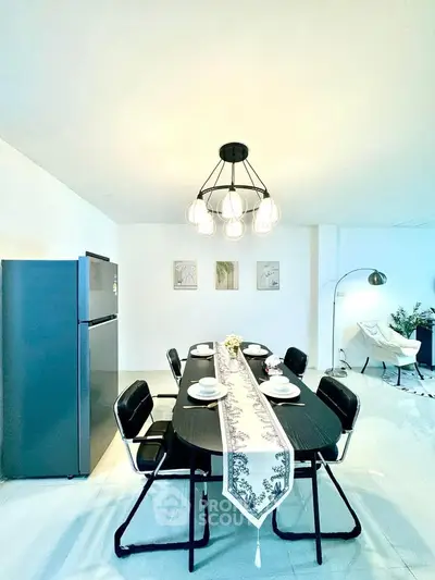 Modern dining area with elegant chandelier and sleek black furniture in a bright, open space.