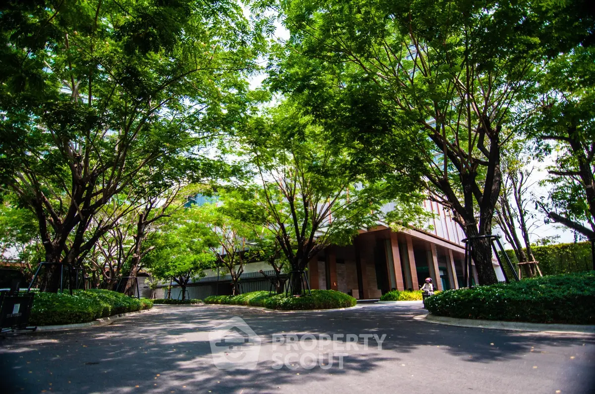 Lush green garden entrance with tall trees and modern architecture.