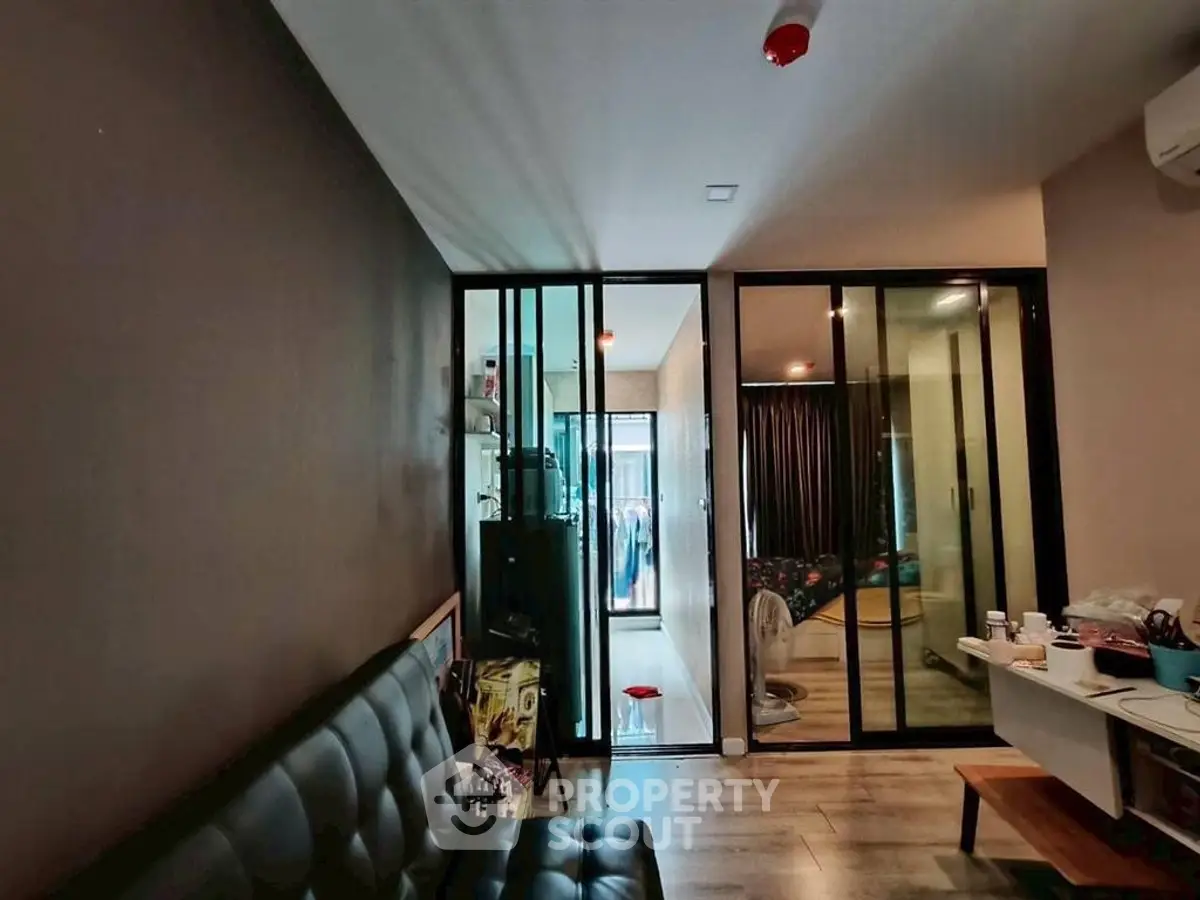 Modern living room with glass partition and sleek furnishings in urban apartment.