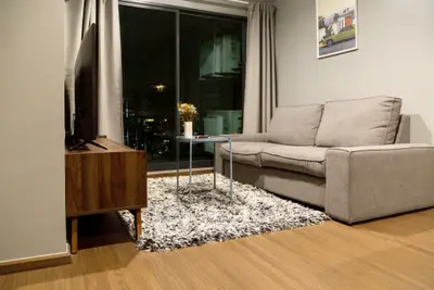 Modern living room with cozy gray sofa, stylish wooden TV stand, and city view through large window.