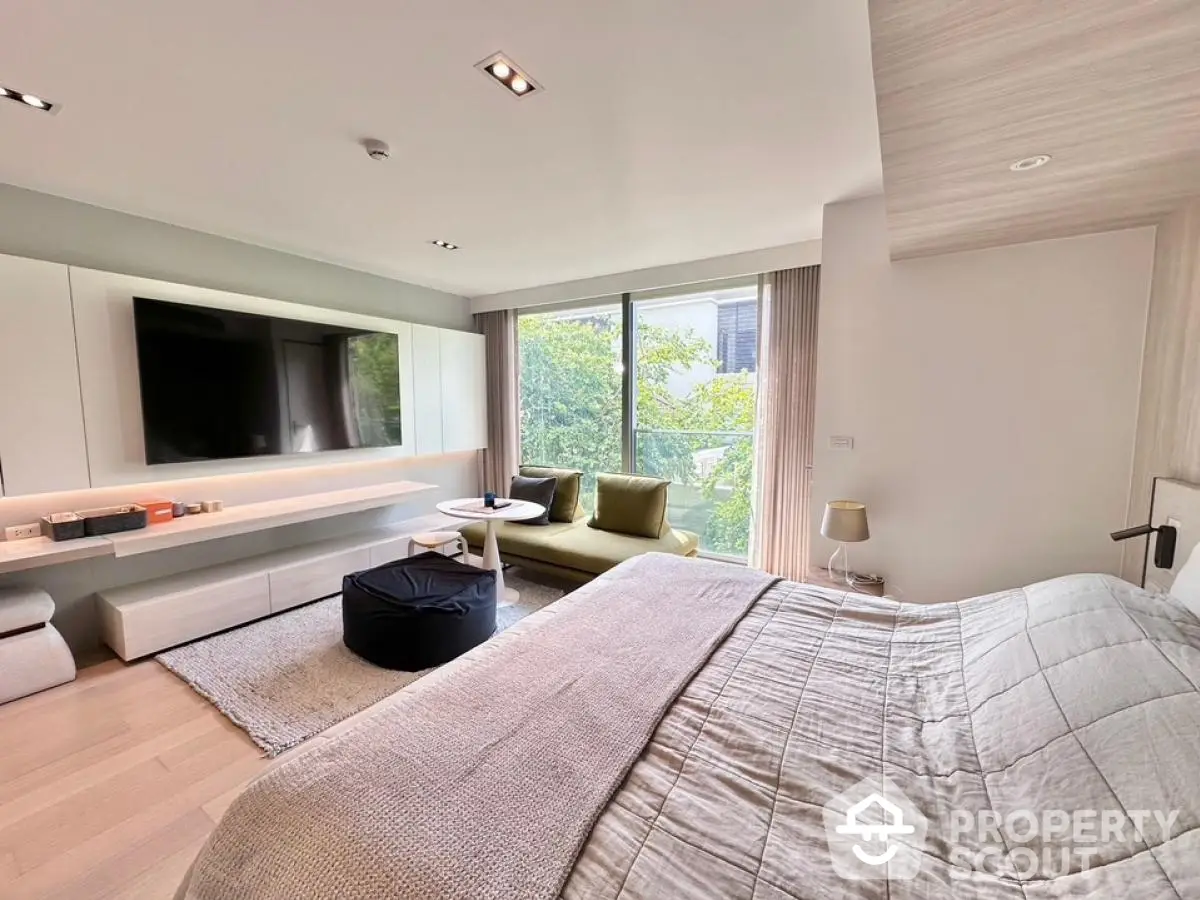 Luxurious bedroom with modern decor and large TV, featuring a cozy seating area and natural light.