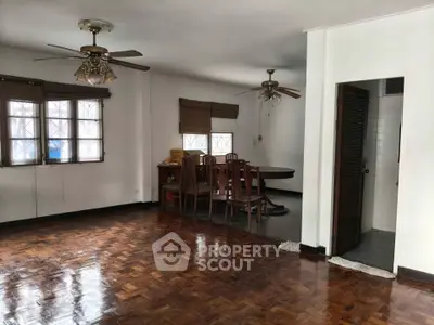 Spacious living room with wooden flooring and dining area, featuring ceiling fans and natural light.