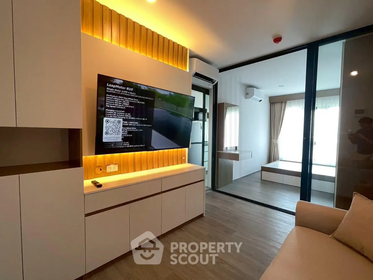 Modern living room with sleek design and large TV, featuring sliding glass doors leading to a bright bedroom.