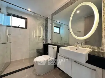 Modern bathroom with glass shower, illuminated mirror, and sleek fixtures.