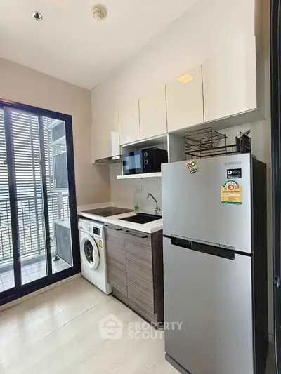 Modern compact kitchen with washing machine and balcony access in urban apartment.