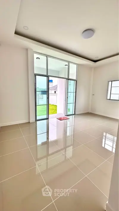 Spacious living room with glossy tiled floors and large windows opening to a garden view.